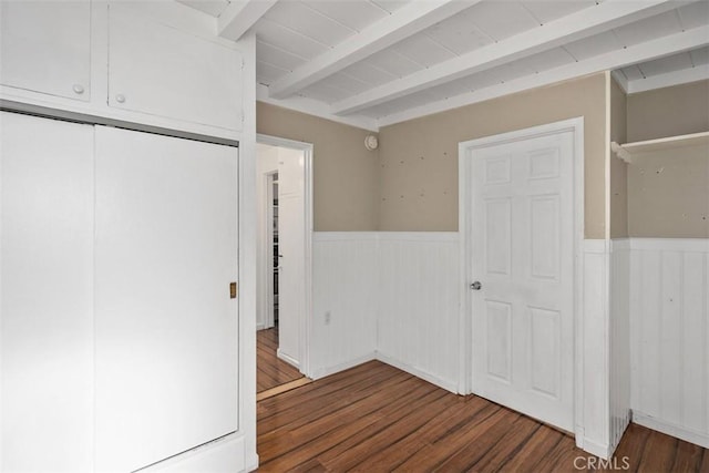 unfurnished bedroom featuring a wainscoted wall, a closet, wood finished floors, and beam ceiling