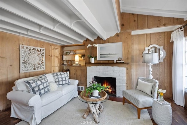 living area featuring vaulted ceiling with beams, a fireplace, visible vents, wood walls, and wood finished floors