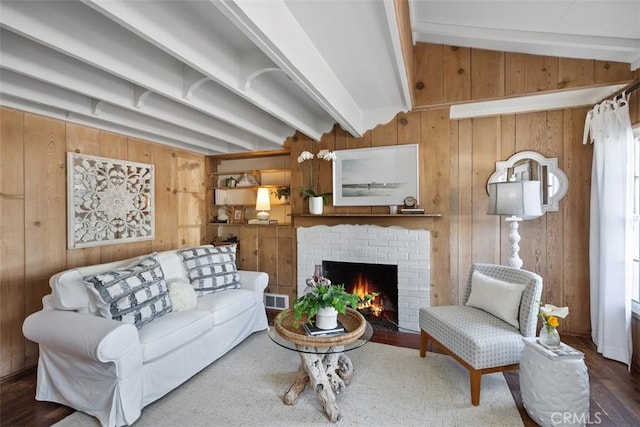 living area with wood walls, visible vents, a brick fireplace, vaulted ceiling with beams, and wood finished floors