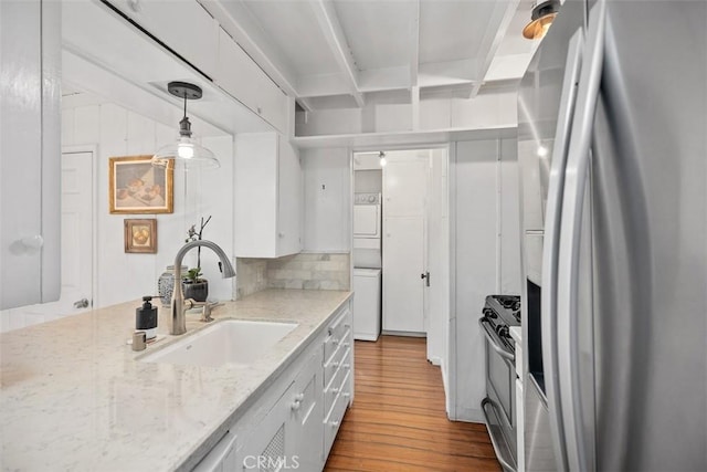 kitchen featuring white cabinets, stacked washer / drying machine, stainless steel appliances, wood finished floors, and a sink