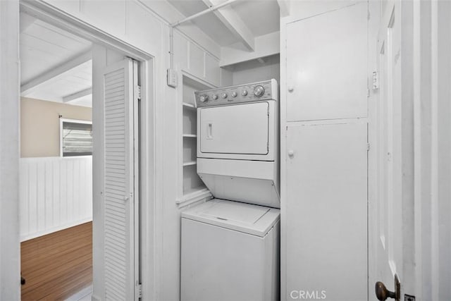clothes washing area with stacked washer and clothes dryer, wood finished floors, laundry area, and wainscoting
