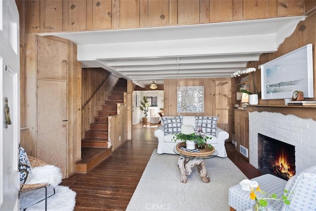 living room with stairs, a brick fireplace, wooden walls, and beamed ceiling