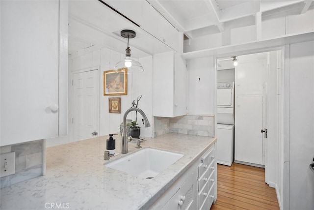 kitchen with white cabinets, light wood-style floors, stacked washer / dryer, and a sink