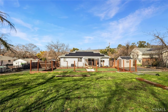 back of house featuring a fenced backyard, an outdoor structure, solar panels, and a lawn