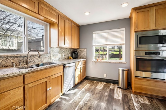 kitchen with appliances with stainless steel finishes, hardwood / wood-style floors, sink, backsplash, and light stone countertops