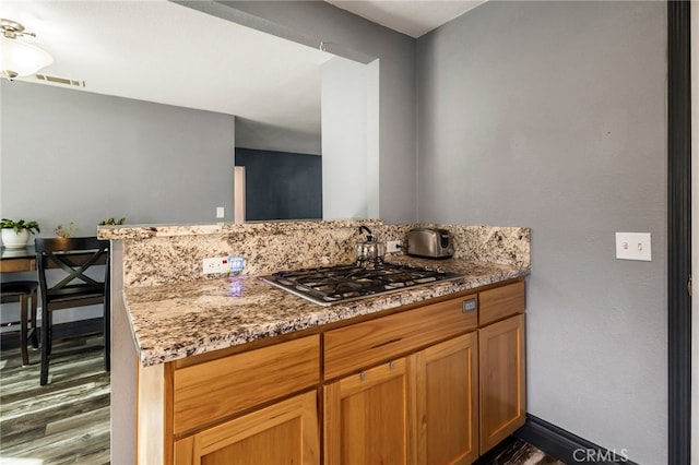 kitchen featuring dark wood-type flooring, kitchen peninsula, stainless steel gas stovetop, and stone countertops