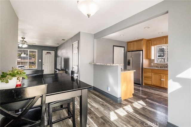 kitchen with a wealth of natural light, stainless steel refrigerator with ice dispenser, dark wood-type flooring, and baseboards