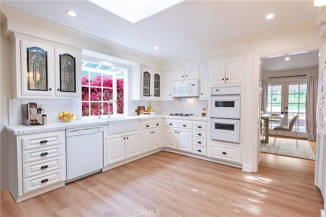 kitchen featuring white appliances, light wood finished floors, white cabinets, glass insert cabinets, and ornamental molding