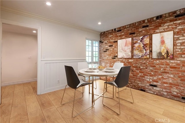 dining area with hardwood / wood-style floors, ornamental molding, wainscoting, brick wall, and baseboards