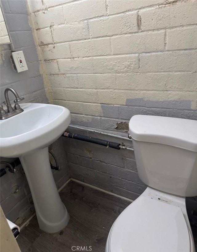 bathroom featuring concrete block wall, toilet, and wood finished floors