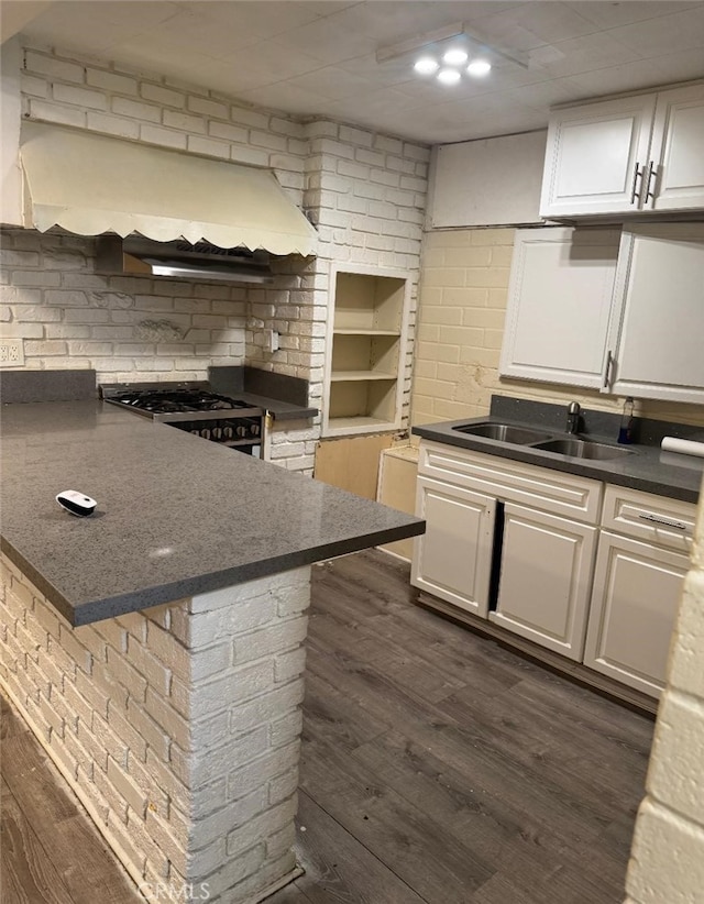 kitchen with dark wood finished floors, custom exhaust hood, dark countertops, white cabinetry, and a peninsula