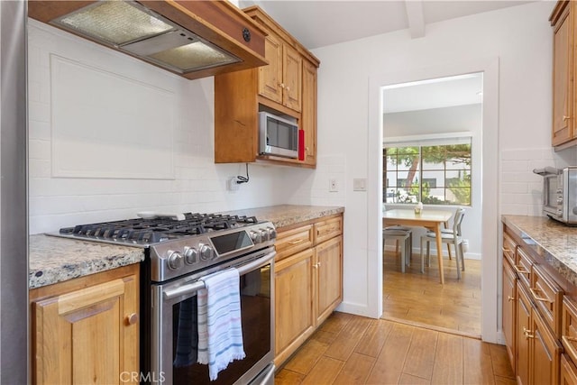 kitchen featuring light stone counters, stainless steel appliances, tasteful backsplash, custom range hood, and light wood-style floors