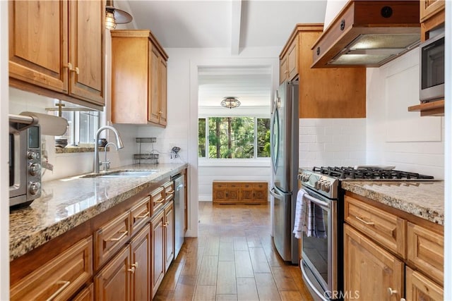 kitchen with appliances with stainless steel finishes, extractor fan, a sink, and light stone countertops