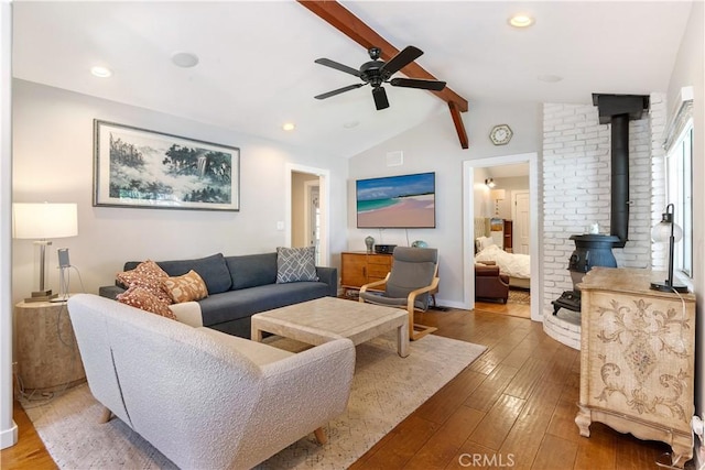 living area featuring recessed lighting, wood-type flooring, lofted ceiling with beams, a wood stove, and ceiling fan