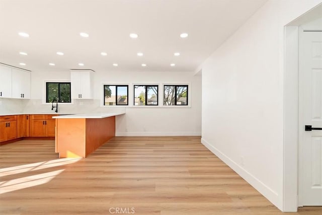 kitchen featuring a breakfast bar, white cabinetry, light wood-type flooring, kitchen peninsula, and backsplash