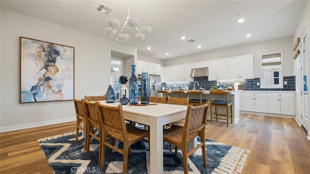 dining area with sink, a chandelier, and light wood-type flooring