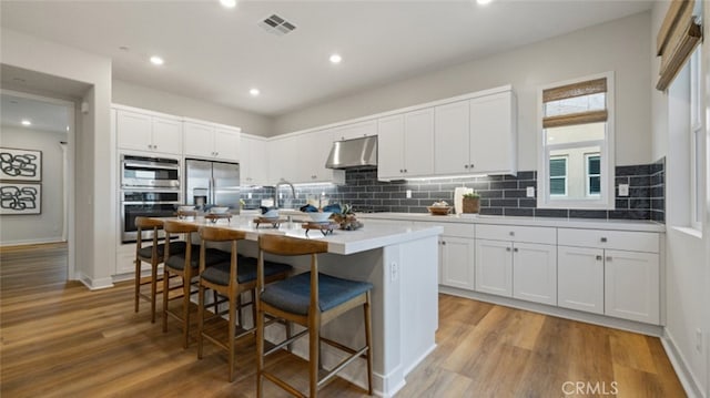 kitchen with a breakfast bar area, light hardwood / wood-style flooring, a kitchen island with sink, stainless steel appliances, and white cabinets