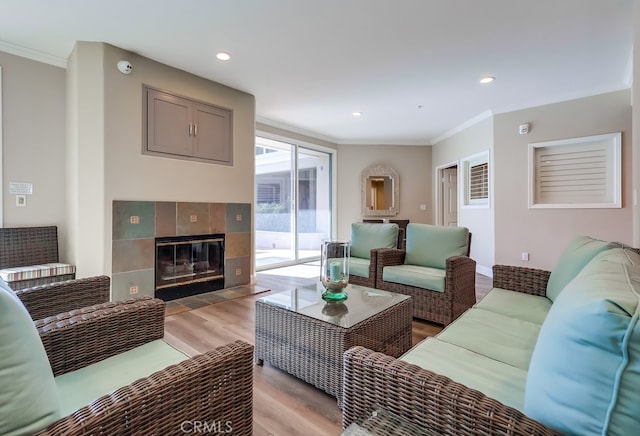 living room with crown molding, a tiled fireplace, and light hardwood / wood-style flooring