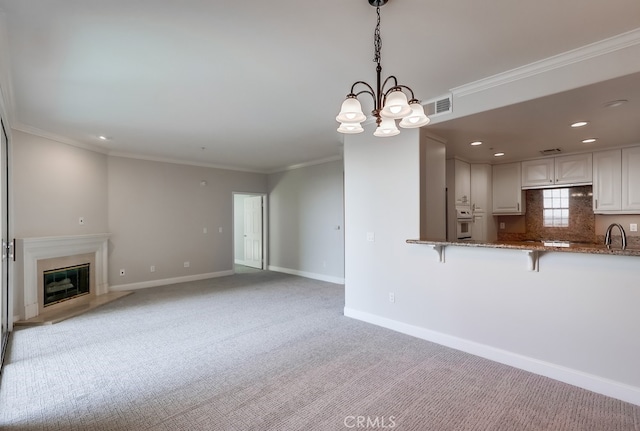 unfurnished living room with a fireplace, sink, ornamental molding, light carpet, and an inviting chandelier