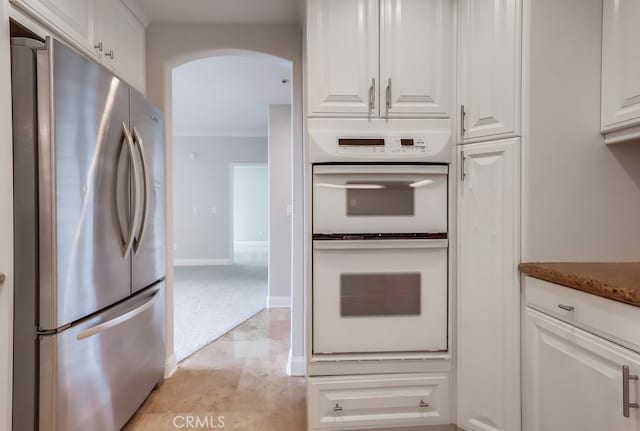 kitchen with white cabinetry, stainless steel fridge, white double oven, and dark stone counters