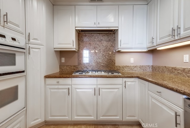 kitchen with white appliances, light stone countertops, and white cabinets