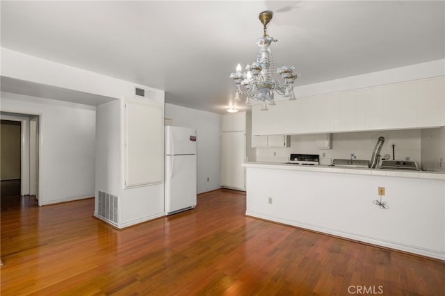 kitchen featuring white cabinetry, a chandelier, white refrigerator, pendant lighting, and hardwood / wood-style floors