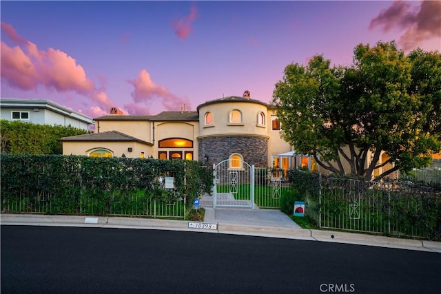 mediterranean / spanish-style home with stone siding, a fenced front yard, a gate, and stucco siding