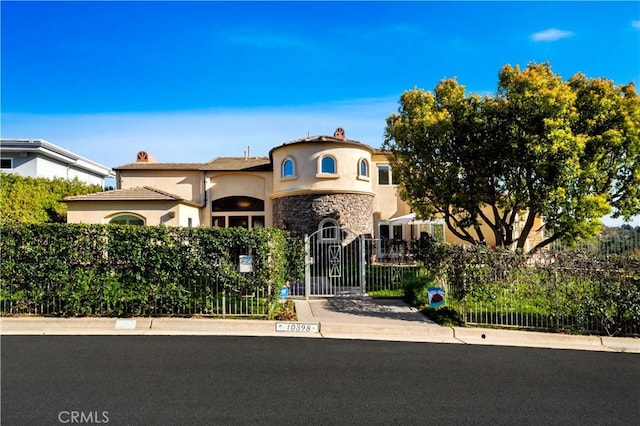 mediterranean / spanish-style home with a fenced front yard, a gate, stone siding, and stucco siding