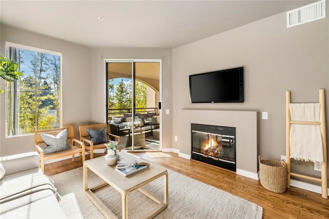 living room with baseboards, visible vents, wood finished floors, and a glass covered fireplace