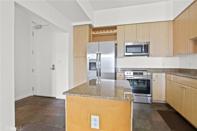 kitchen with appliances with stainless steel finishes, light brown cabinetry, a kitchen island, and dark stone counters