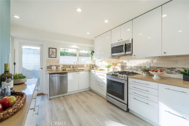 kitchen with sink, white cabinetry, light hardwood / wood-style flooring, stainless steel appliances, and backsplash