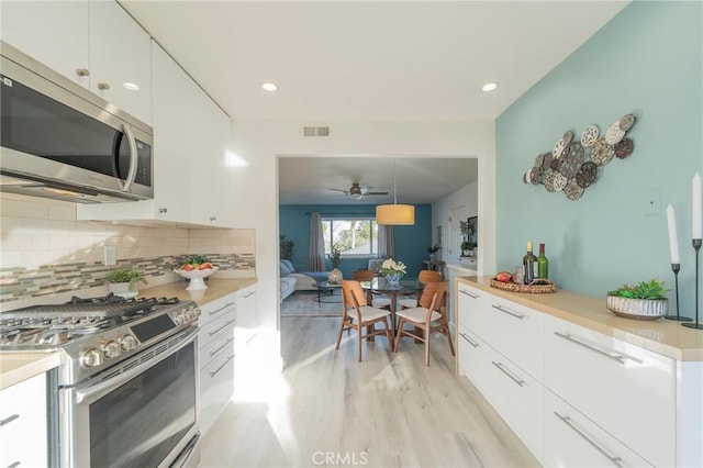 kitchen with appliances with stainless steel finishes, decorative light fixtures, tasteful backsplash, white cabinetry, and light hardwood / wood-style flooring