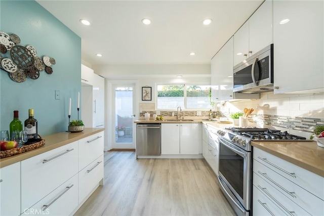 kitchen with decorative backsplash, appliances with stainless steel finishes, light hardwood / wood-style flooring, and white cabinets