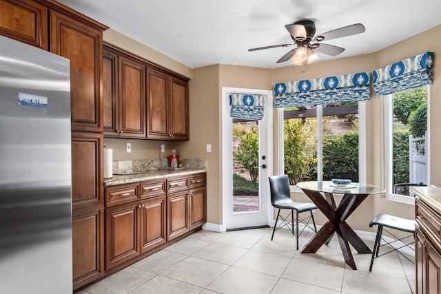 kitchen with light stone counters, light tile patterned floors, stainless steel fridge, and ceiling fan