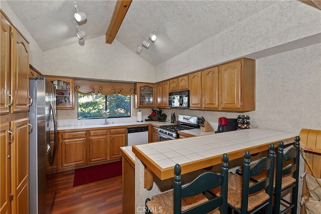 kitchen with a breakfast bar area, appliances with stainless steel finishes, vaulted ceiling with beams, tile countertops, and kitchen peninsula