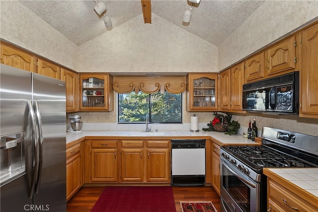 kitchen featuring lofted ceiling, sink, stainless steel appliances, dark hardwood / wood-style flooring, and tile countertops