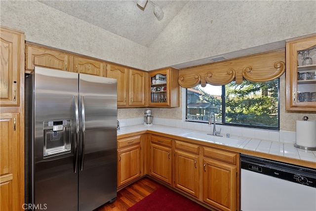 kitchen featuring white dishwasher, sink, tile counters, and stainless steel refrigerator with ice dispenser