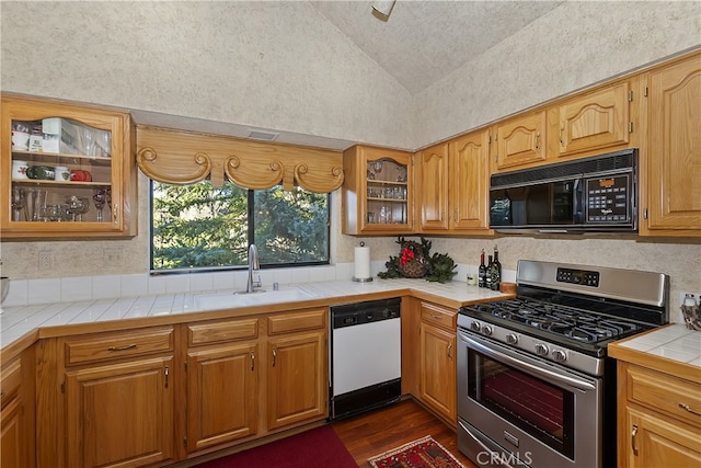 kitchen featuring lofted ceiling, sink, tile counters, white dishwasher, and stainless steel gas range