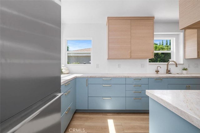 kitchen with blue cabinetry, sink, stainless steel refrigerator, and light wood-type flooring