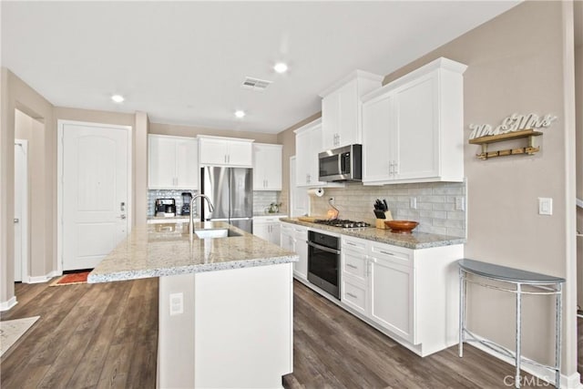 kitchen featuring an island with sink, white cabinets, light stone counters, stainless steel appliances, and dark wood-type flooring