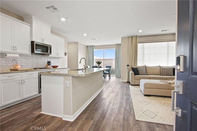 kitchen with sink, backsplash, light stone countertops, an island with sink, and white cabinets