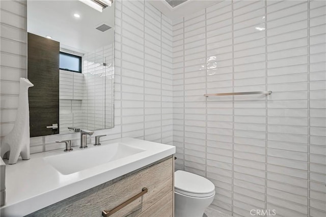 bathroom featuring tile walls, vanity, a shower, and toilet