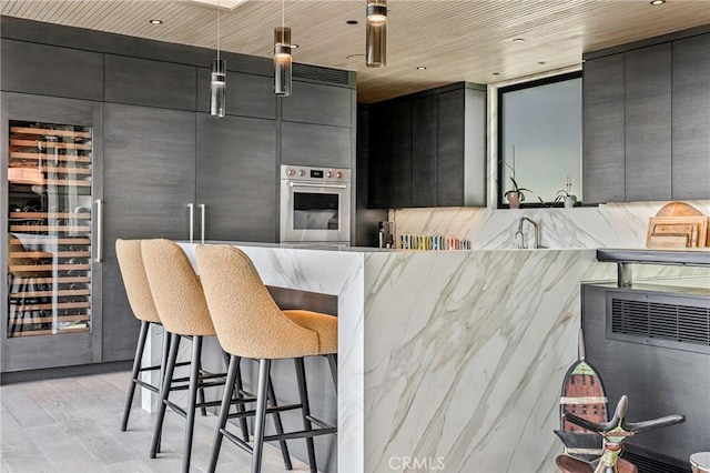 kitchen with sink, a breakfast bar area, stainless steel oven, wood ceiling, and light wood-type flooring