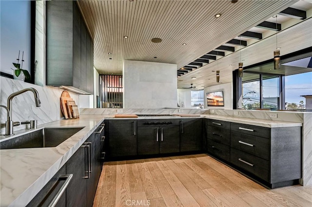 kitchen featuring sink, light hardwood / wood-style flooring, kitchen peninsula, light stone countertops, and decorative backsplash