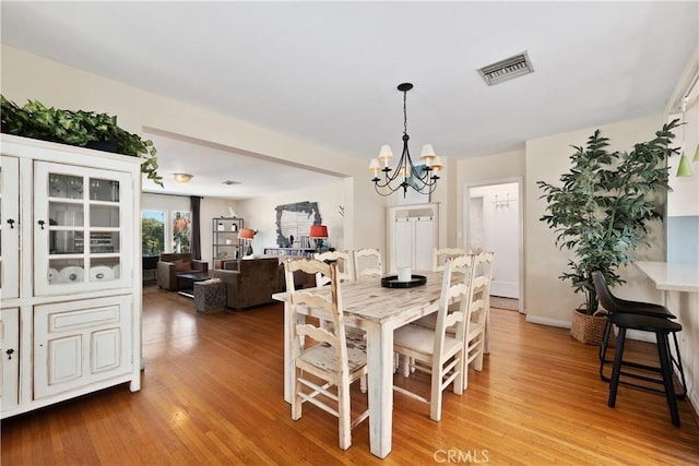 dining room with light wood-type flooring, visible vents, baseboards, and an inviting chandelier