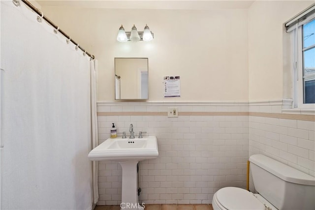 full bath featuring a shower with curtain, a wainscoted wall, tile walls, and toilet