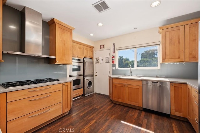 kitchen featuring stainless steel appliances, stacked washer / drying machine, visible vents, a sink, and wall chimney exhaust hood