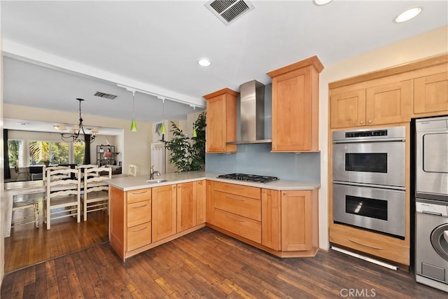 kitchen featuring stainless steel appliances, visible vents, stacked washer / dryer, a sink, and wall chimney exhaust hood