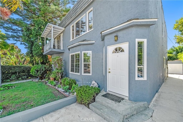 view of exterior entry featuring a lawn, a balcony, and stucco siding