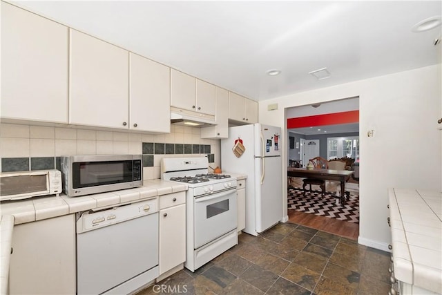 kitchen with white appliances, tile counters, decorative backsplash, under cabinet range hood, and white cabinetry